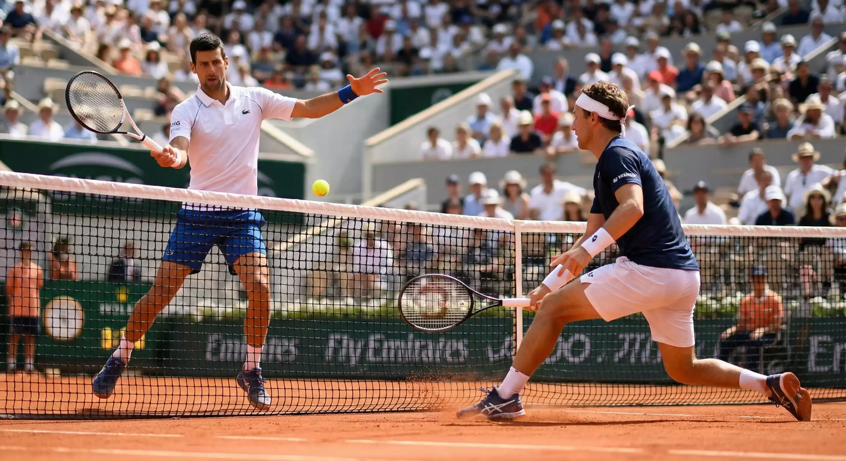 Intercambio de golpes entre dos tenistas en pista de tierra batida con polvo naranja visible